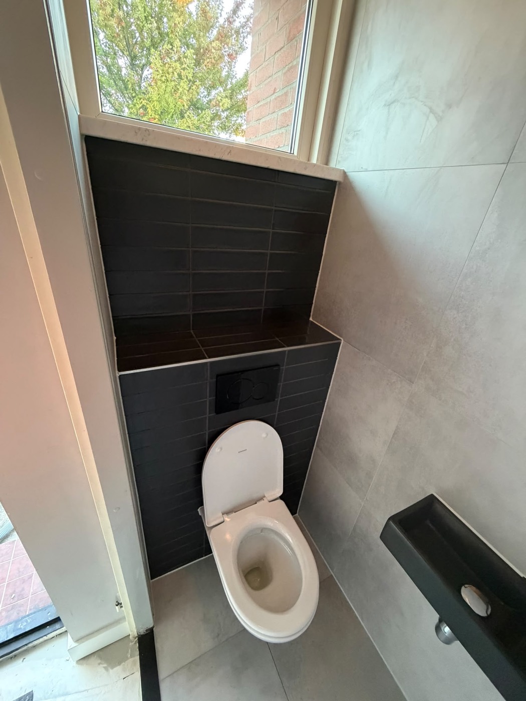 Toilet renovatie in Alphen aan den Rijn met zwarte tegelwand, zwevend toilet en raam – Groene Hart Badkamers