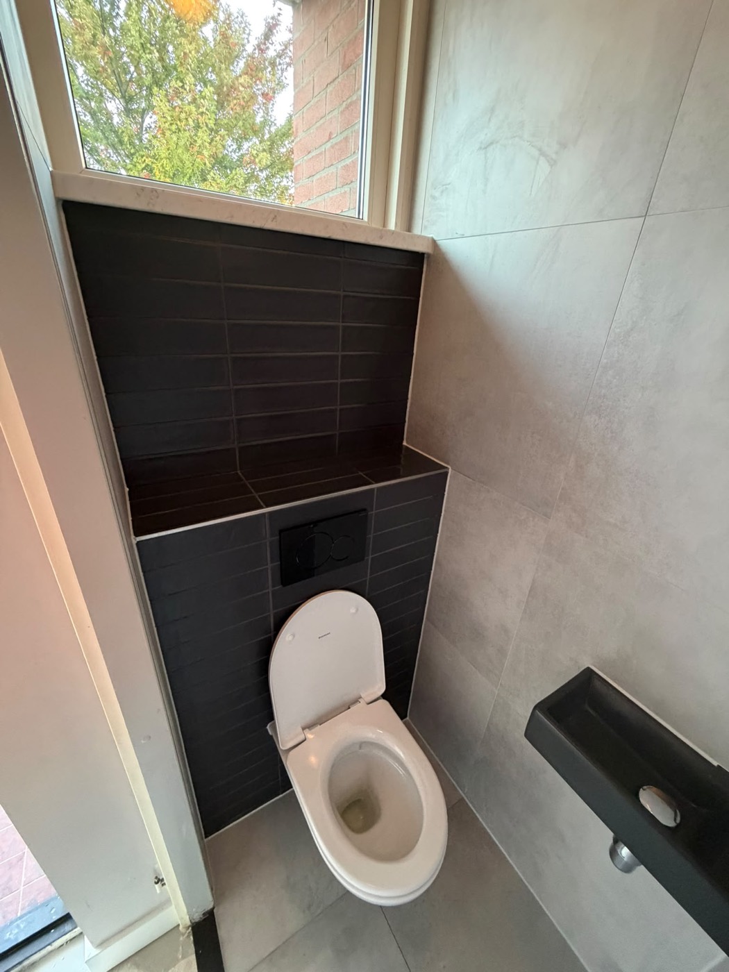 Zijaanzicht van het vernieuwde toilet in Alphen aan den Rijn, zwarte tegels tot onder het raam