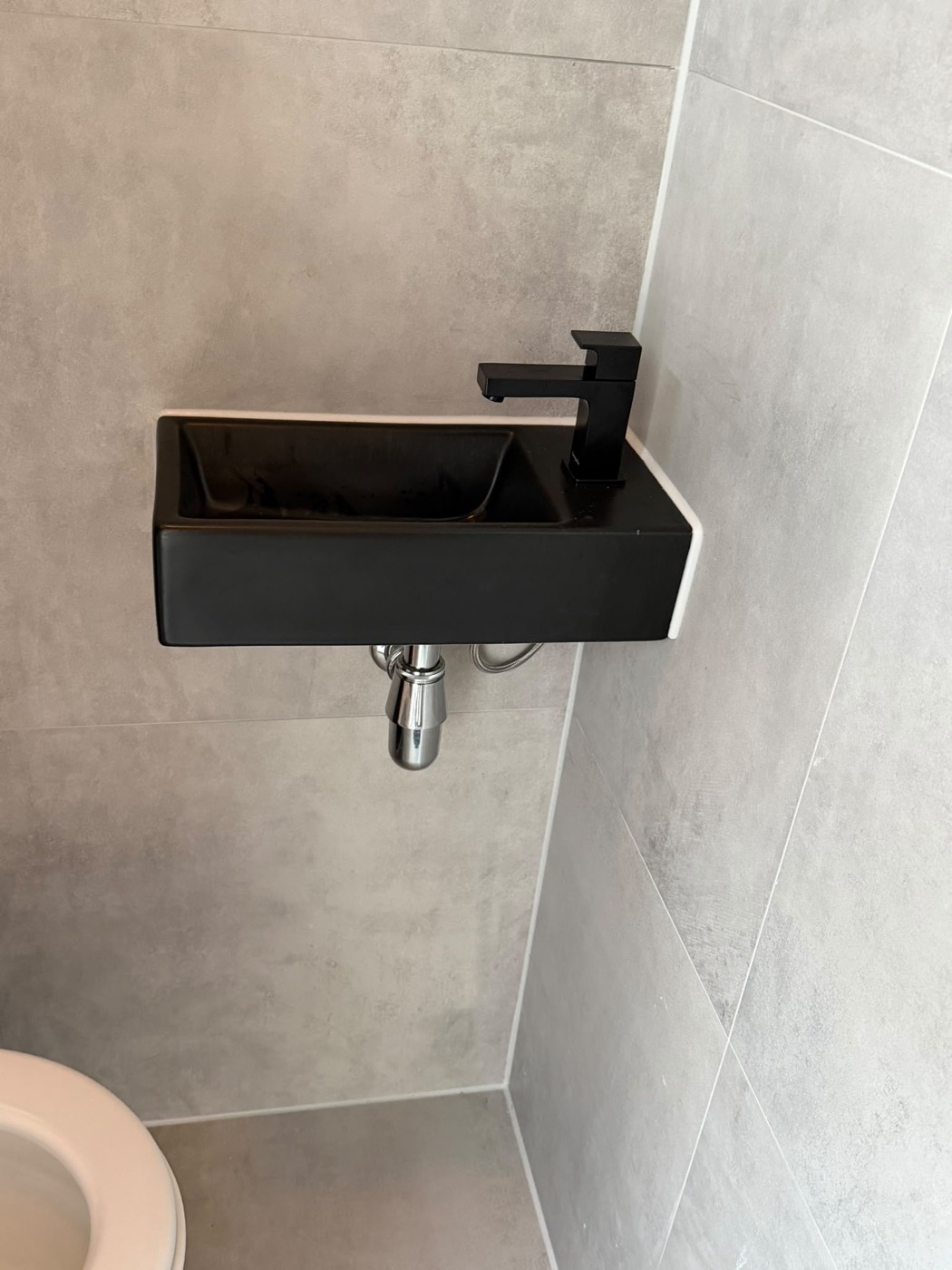 Zijaanzicht van de design wastafel tegen de grijze tegelwand, toilet renovatie Alphen aan den Rijn