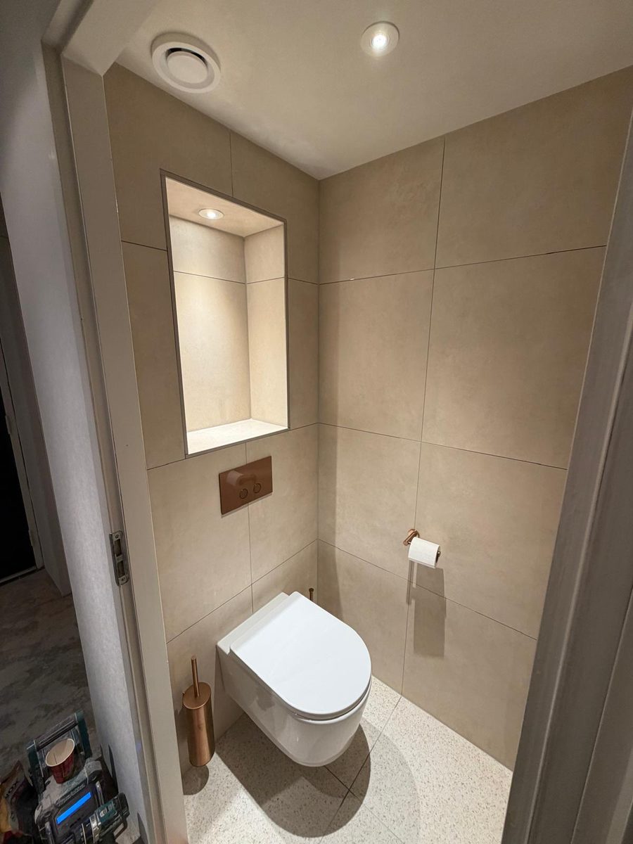 Compact toilet met zandkleurige tegels, zwevend toilet, verlichte nis en bronzen details